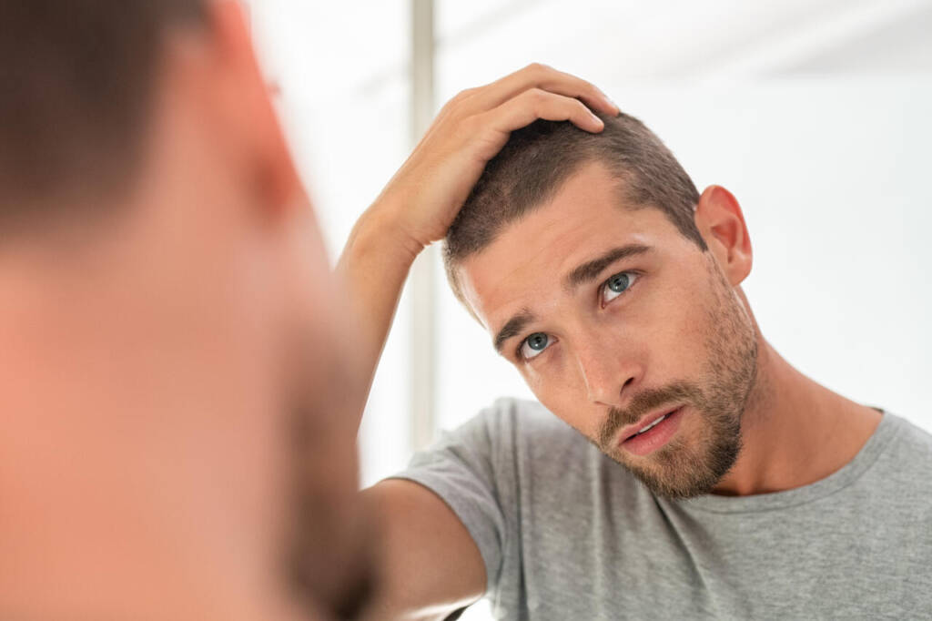 Young,Unshaven,Man,Looking,At,Mirror,In,Bathroom,At,Home.