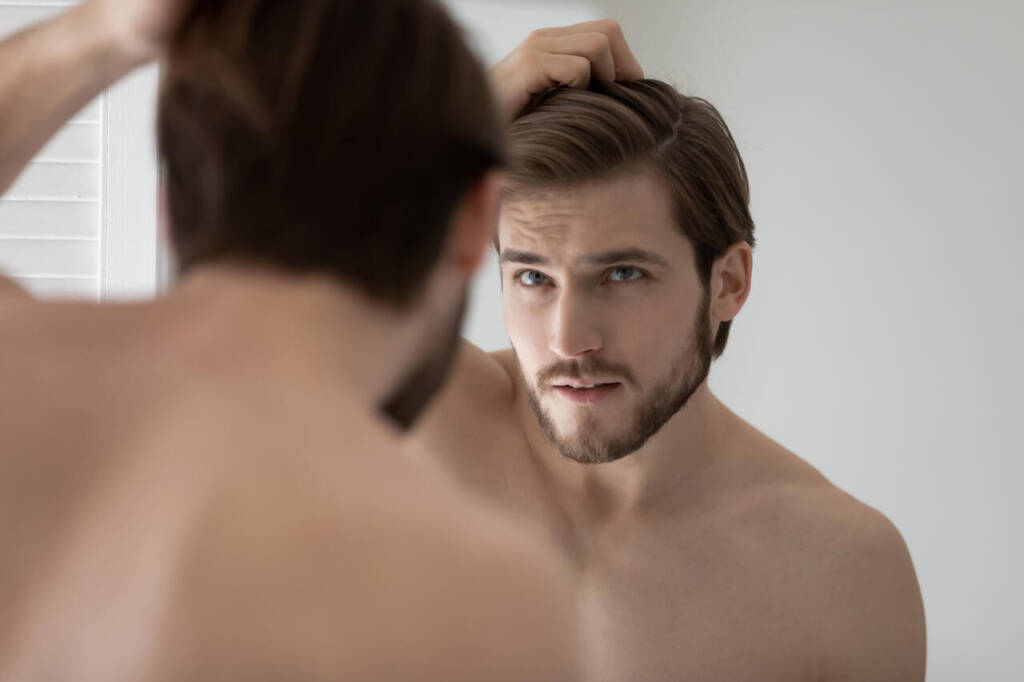 Anxious,Young,Caucasian,Man,Look,In,Mirror,In,Bathroom,Touch